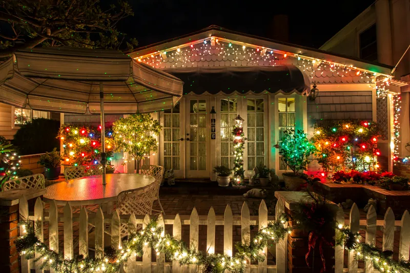 Cottage porch at night with multicolor Christmas lights along the roof edge and garland on the fence